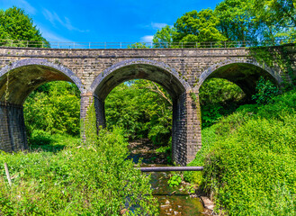 Fototapeta premium A view towards a three arched a bridge across the River Goyt at New Mills, High Peak in the UK in summertime 