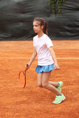 Girl playing tennis on a clay court holding a red tennis racket