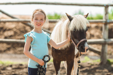 Cute little girl petting a pony in a farm