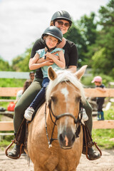 Cute little girl riding horse with her mother