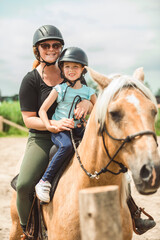 Cute little girl riding horse with her mother
