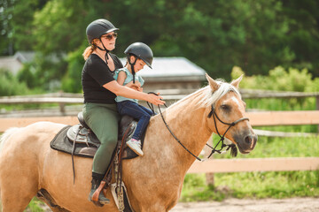 Cute little girl riding horse with her mother