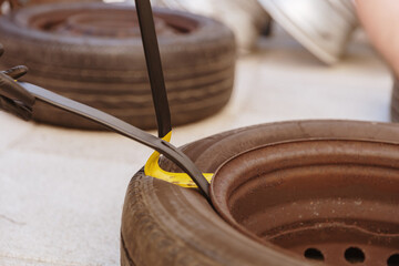 A man's hands use a crowbar to disassemble a car tire.