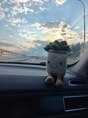 Cute plush succulent toy on dashboard during a scenic drive at dusk on an open road