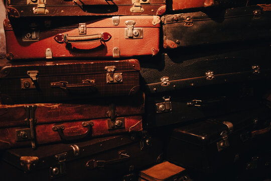 A stack of old, worn suitcases in warm lighting. The image evokes themes of memory, migration, and the passage of time.