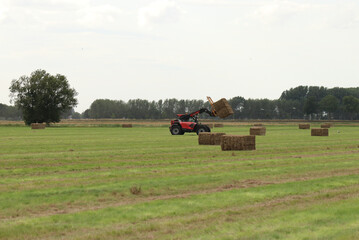a green hay field with large bales and a telescopic loader in the countryside in summer