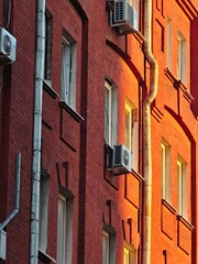 Wall of a red brick building illuminated by warm evening sunlight with air conditioning units