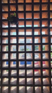 View of a cityscape through a traditional cobog&oacute; hollow brick wall, with a hanging plant. The sunlight creates beautiful patterns of light and shadow on warm-toned terracotta structure. Mercado Novo.
