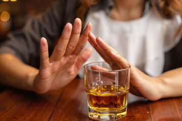 Woman refusing whiskey while sitting at a wooden table in a bar  