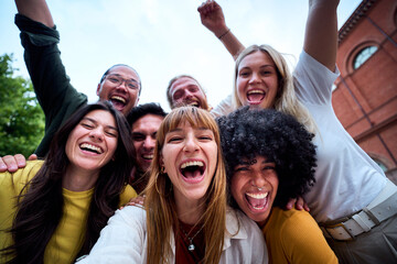 Cheerful multi-ethnic young students celebrating success with arms raised and joyful screams, creating an atmosphere of excitement and unity in front of their university campus