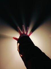 Hand reaching out in the dark with radiant light shining from behind at an artistic exhibition