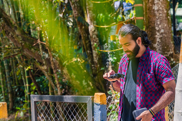 Man in plaid shirt with tied hair photographing nature with phone in lush Colombian forest near...