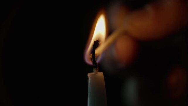 Hand grips wooden match striking paraffin candle on dark room backdrop closeup