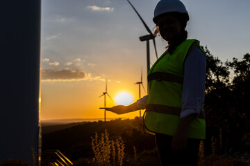Female engineer holding smartphone at wind farm during sunset