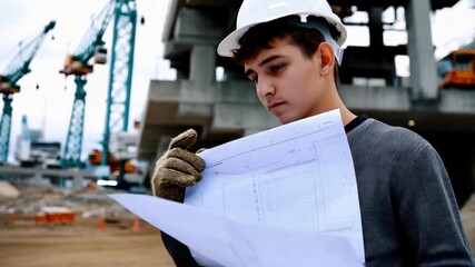 Young construction worker analyzing blueprints at a building site - Powered by Adobe