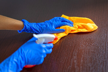 Person Cleaning Surface with Gloves and Cloth. Close-up of hands wearing blue gloves using spray...