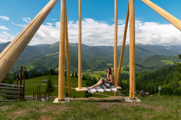 Woman reading on swing with mountain view. A woman sits on a large wooden swing, reading a book and...