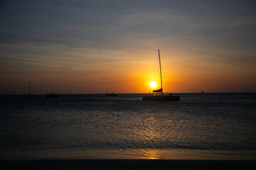 Golden sunset over the ocean with a sailboat anchored near the shore