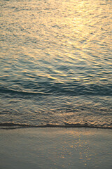 Soft sun rays reflect on calm ocean waves at sunset on a serene beach