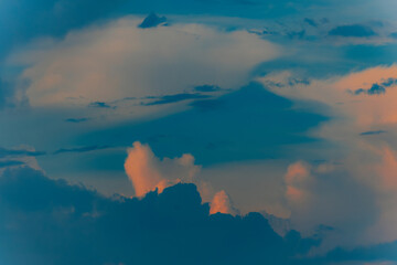 Dramatic cumulus clouds lit by golden sunset light against a darkening blue sky, creating a moody...