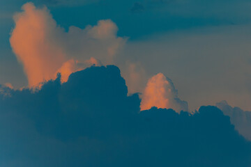 Dramatic cumulus clouds lit by golden sunset light against a darkening blue sky, creating a moody...