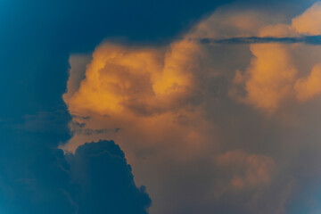 Dramatic cumulus clouds lit by golden sunset light against a darkening blue sky, creating a moody...