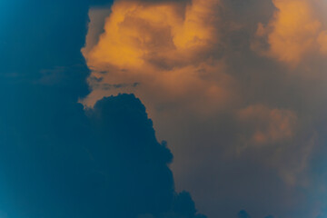 Dramatic cumulus clouds lit by golden sunset light against a darkening blue sky, creating a moody...