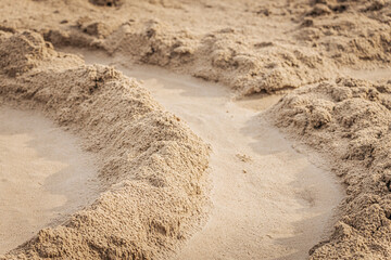 Close-up view of curved sand mounds forming a winding path on a sunlit beach, showcasing fine texture and golden tones.