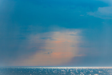 Calm sea sparkles under soft sunlight as gentle rays break through a cloudy sky, casting a peaceful...
