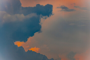 Thick clouds in varying shades of blue and gray are illuminated by soft orange sunset hues,...