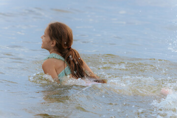 A happy young girl emerges from the water with her eyes shut and a wide smile, causing a big splash...
