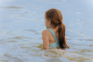 A happy young girl emerges from the water with her eyes shut and a wide smile, causing a big splash...