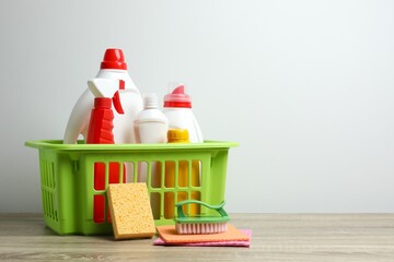 Cleaning supplies in green basket on table, with brushes, spray, bottle, sponge. Ideal for...