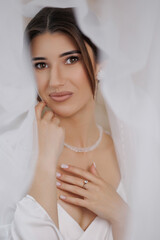Bridal portrait of a woman in white gown with delicate veil and soft makeup in a cozy setting