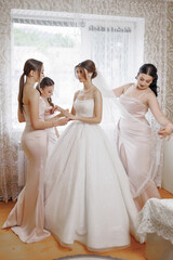 Bride prepares for wedding with friends in elegant dresses in bright room