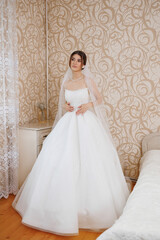 Bride in elegant white gown poses indoors before wedding ceremony
