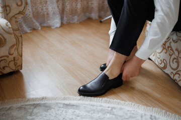 Man getting ready by putting on black shoes in a stylish room during morning hours