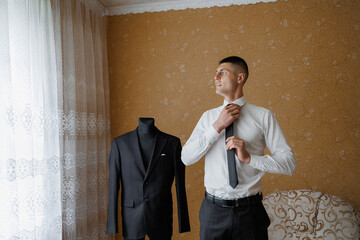 Man adjusts tie while preparing for formal event in cozy room with vintage decor