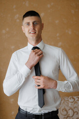 Young man adjusting tie indoors before an event in a stylish outfit