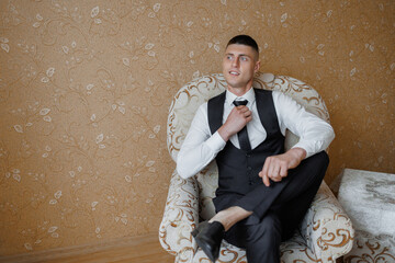 Stylish man adjusting tie while sitting comfortably in chair at home
