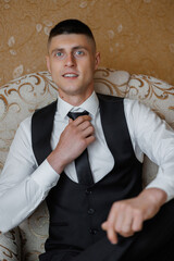 Groom adjusting tie while seated in elegant attire in indoor setting