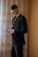 Man adjusting suit jacket in elegant room with lace curtains
