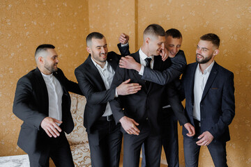 Groom and groomsmen celebrate together before wedding ceremony in warm-toned room