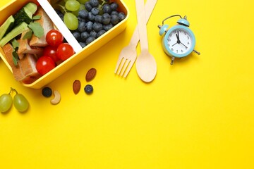 Top view of a healthy lunch box containing fresh fruits, vegetables and nuts accompanied by an alarm clock on a bright green background. Ideal for promoting balanced nutrition