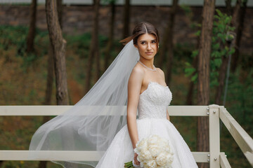 Bride in elegant dress holding bouquet near trees on wedding day in a serene setting