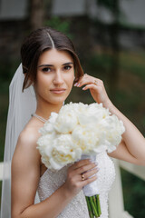 Elegant bride holding a bouquet of white peonies in a serene outdoor setting
