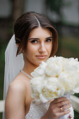 Bride holding a bouquet of white flowers in a serene outdoor setting before the wedding ceremony