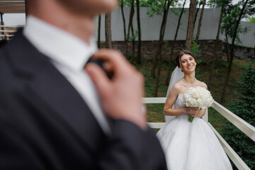 Bride smiles while groom adjusts tie during outdoor wedding ceremony