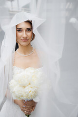 Bride holding bouquet in soft light with veil softly framing her face during wedding preparations