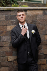 Groom in elegant suit poses confidently against a stone wall during wedding preparations